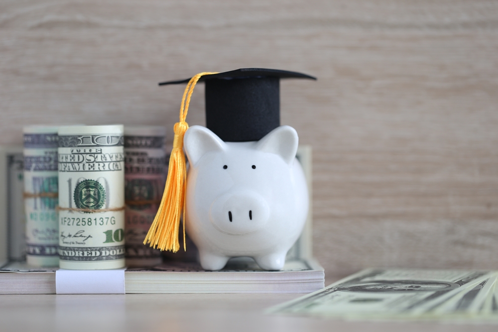 Piggy bank wearing a graduation cap with cash beside it