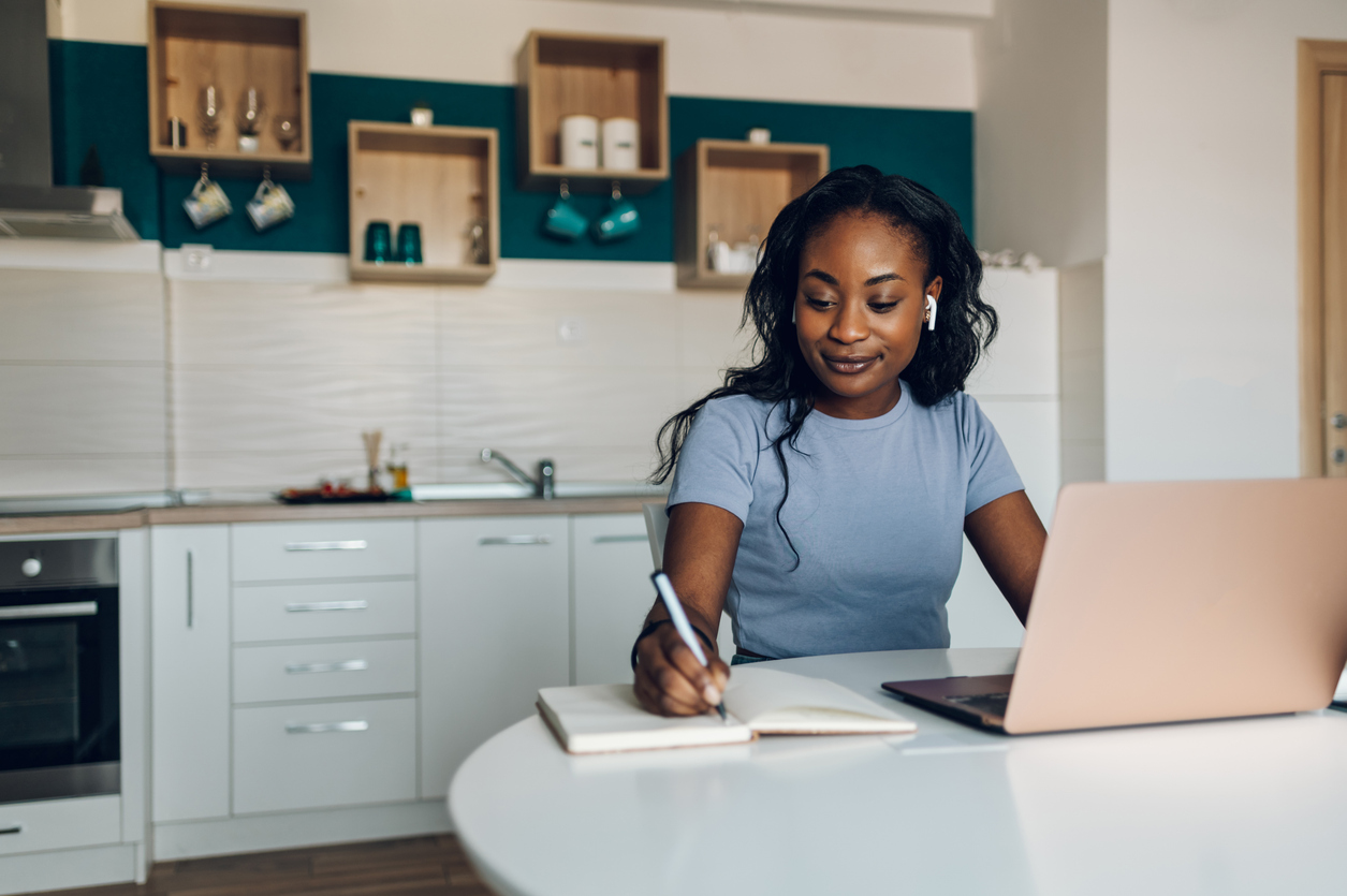 A woman writing in a notebook on her laptop